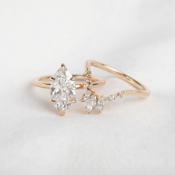 A gold ring set featuring a large marquise-cut clear gemstone and delicate leaf-shaped marquise and round clear gemstones on a soft white background.